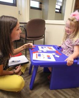 Speech therapy in session, therapist sitting on the floor with a little girl